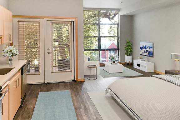 A bedroom with a bed, a couch, a table, and a window with a view of a red building outside.