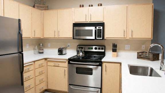 A kitchen with a refrigerator, microwave, oven, sink and cabinets.
