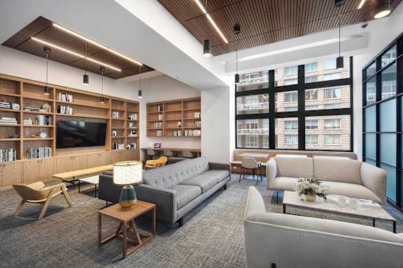 A modern living room with a grey sofa, wooden bookshelves, and a large window.