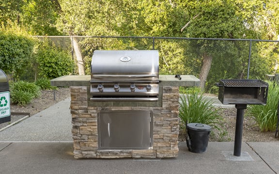 a barbecue grill in a backyard with a trash can