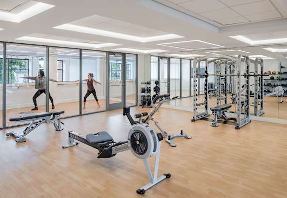 A gym with a row of treadmills and a row of weights at Trio Newton Apartments, Massachusetts, 02460