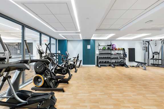 A gym with treadmills, elliptical machines, and other exercise equipment at Trio Newton Apartments, Newton