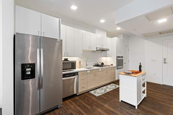 A modern kitchen with a stainless steel refrigerator and wooden flooring. at Trio Newton Apartments, Newton, 02460