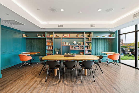 A room with a round table surrounded by chairs and a bookshelf filled with books at Trio Newton Apartments, Newton, Massachusetts