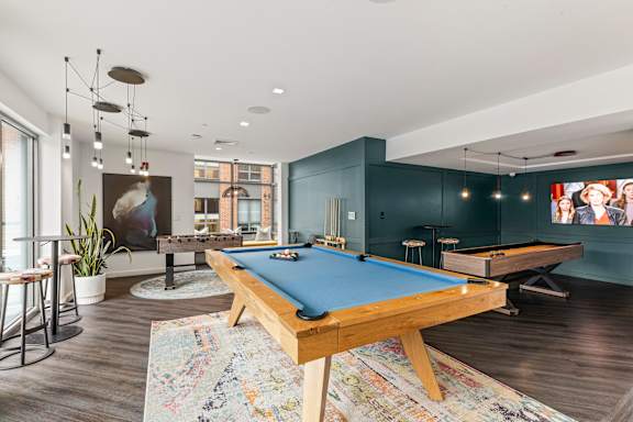A pool table is in the middle of a room with a bar stool and a potted plant at Trio Newton Apartments, Newton, MA, 02460