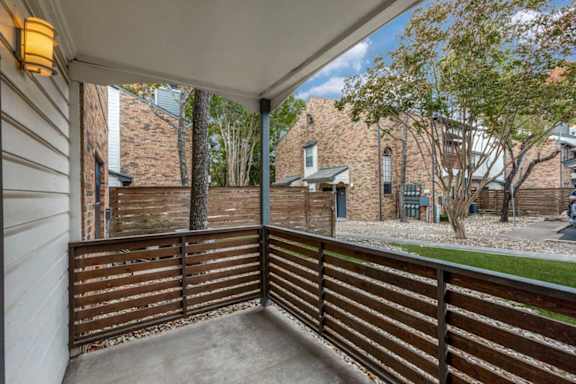 A balcony with a wooden railing and a view of a backyard with a tree and a house.