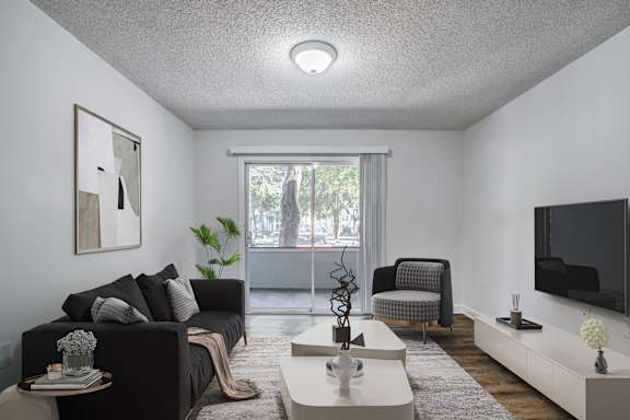 A living room with a grey couch, a white coffee table, and a flat screen TV mounted on the wall.