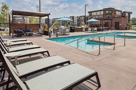 A pool area with sun loungers and a building in the background.