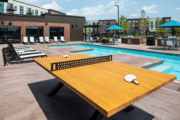 A ping pong table is set up on a patio next to a pool.