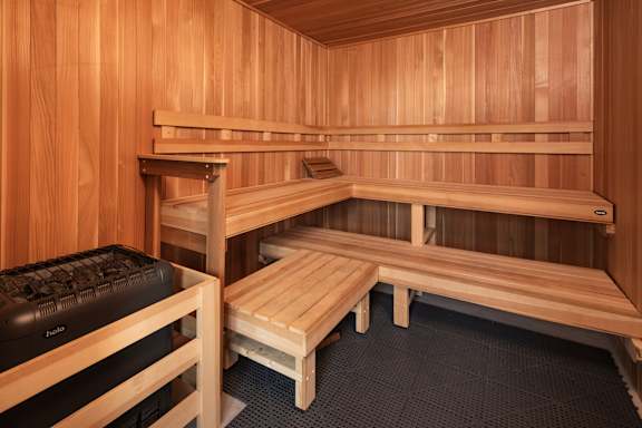 A wooden sauna room with benches and a cooler.
