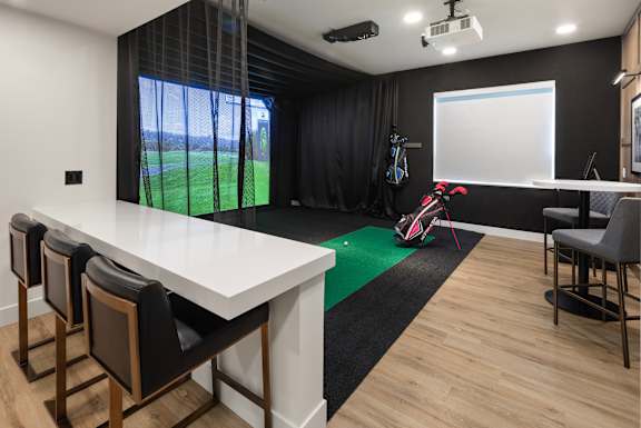 A room with a long table and chairs, a whiteboard, and a golf simulator.
