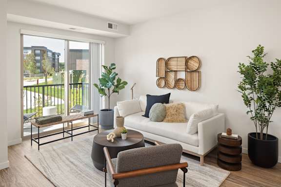 A living room with a white couch, a grey armchair, a coffee table, and a large window with a view of a building.