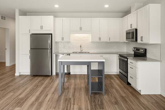 A modern kitchen with white cabinets and a wooden floor.