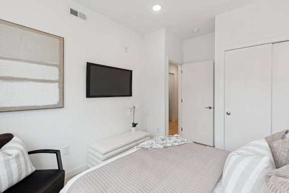 A bedroom with a bed, a chair, and a television mounted on the wall.