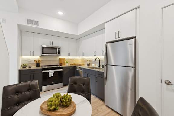 A modern kitchen with a stainless steel refrigerator and black chairs.