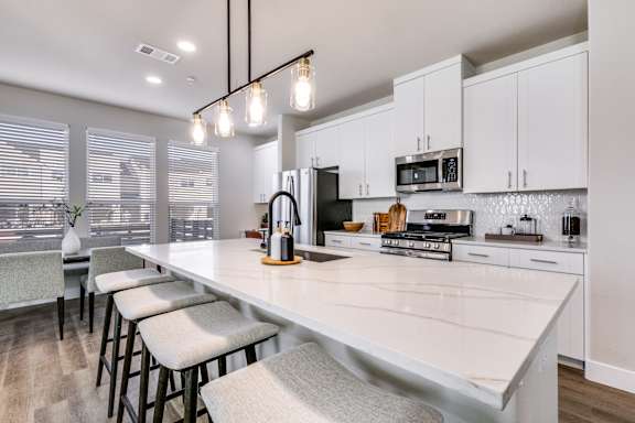 A kitchen with white cabinets and a long island with bar stools.