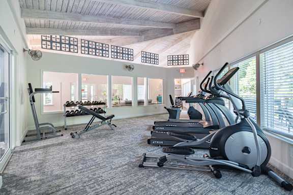 A gym with a row of treadmilers and a weight rack.