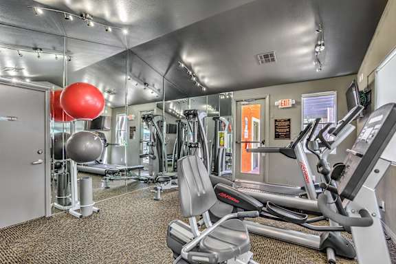 A gym with a variety of equipment including treadmills, weights, and a red exercise ball.