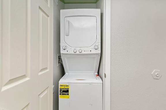 A white washing machine is in a small space between a door and a wall.