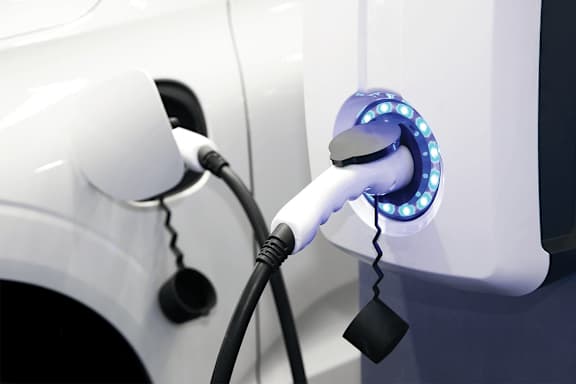 A white car is being charged by a blue lighted electricity plug.