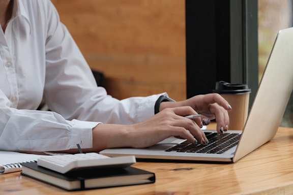 A person in a white shirt is typing on a laptop.