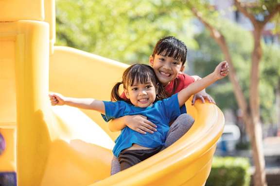 Two children are playing on a yellow slide.