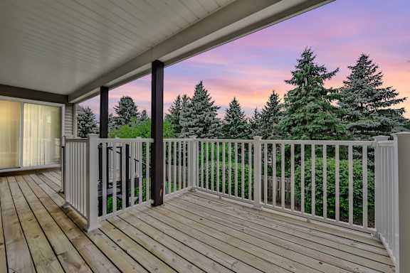 A wooden deck with a white railing and a view of trees.