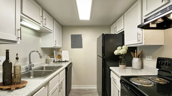 A kitchen with a black refrigerator and white cabinets.