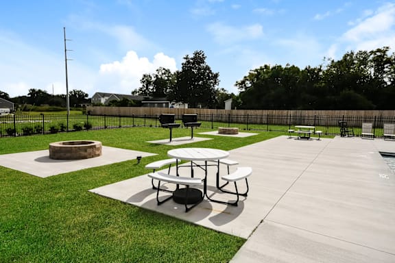 Picnic tables and a fire pit are set up on a concrete patio.