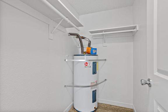 A white wall with a water heater and a pipe.