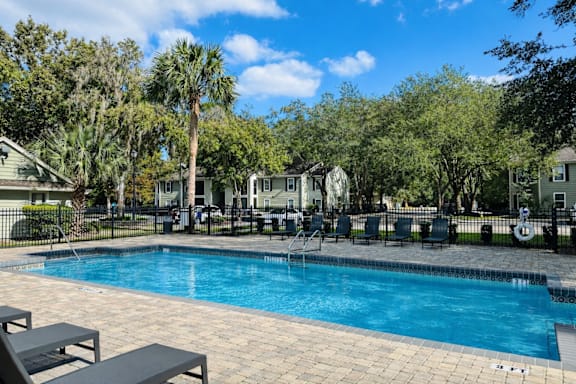 A swimming pool surrounded by trees and chairs.