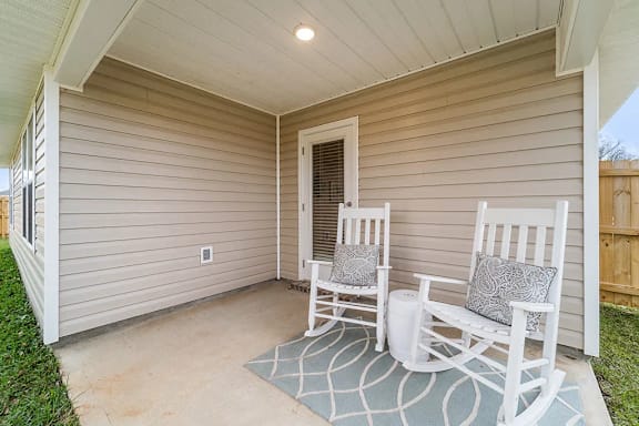 Two white chairs are placed on a rug in front of a house.