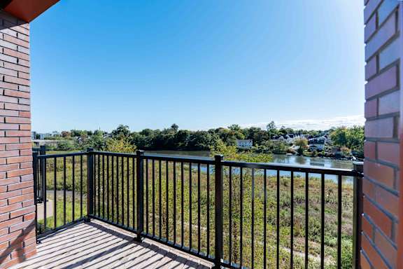 A balcony with a black railing overlooks a body of water and greenery.