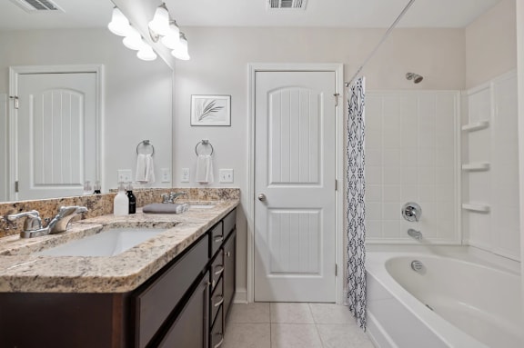A bathroom with a marble countertop and a white tub.