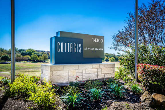 A sign for Cottages at Wells Branch stands in front of a blue sky.