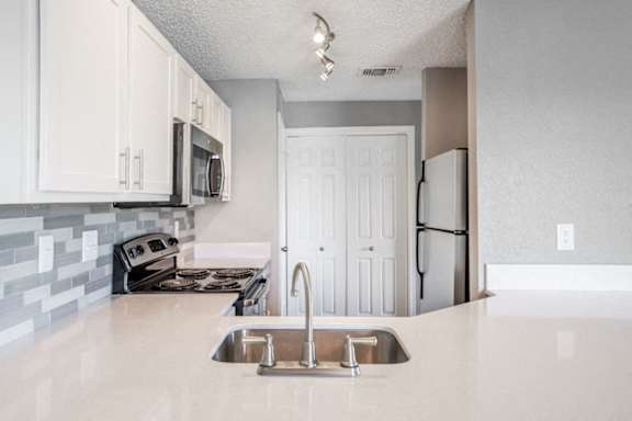 A kitchen with a sink, stove, and cabinets.