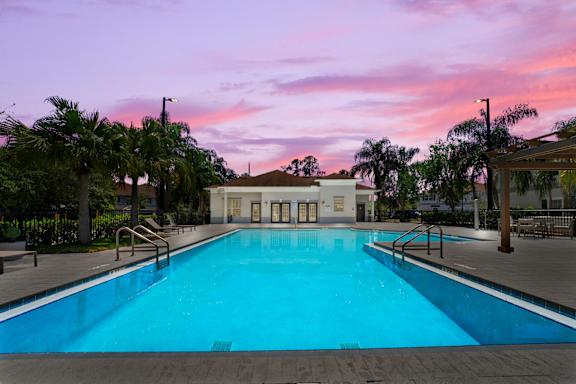 Pet-Friendly Townhomes in Kissimmee, FL – Estates at Lake Cecile - A large swimming pool surrounded by palm trees and a building in the background.