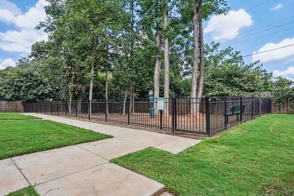 A black fence surrounds a green lawn with a sidewalk and trees.