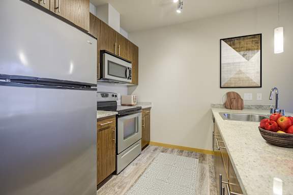 A kitchen with a refrigerator, microwave, oven, sink, and a bowl of apples on the counter.