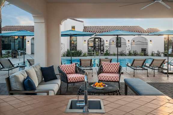 A patio with a table, chairs, and a pool in the background.