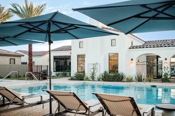 A pool with a blue umbrella and chairs.
