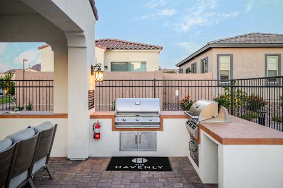 A patio with a grill and chairs is set up on a balcony.