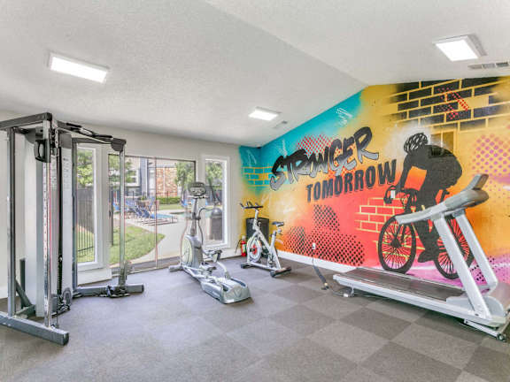 A gym with a wall mural that says "Stronger Tomorrow" and a treadmill.