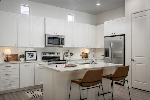 A kitchen with white cabinets and a countertop with two chairs.