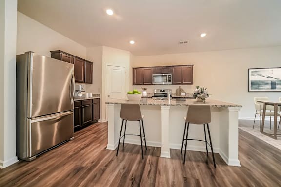 A kitchen with a refrigerator, bar stools, and a countertop.