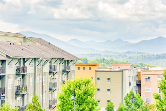 a row of apartment buildings with trees in the foreground and mountains in the background