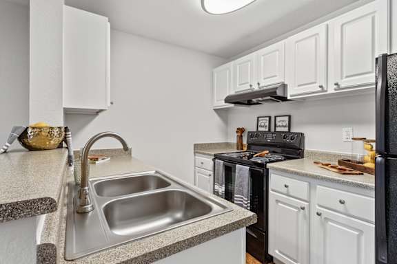 A kitchen with a black refrigerator and white cabinets.
