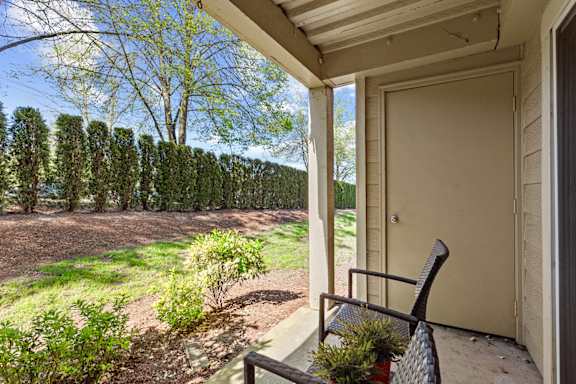A chair sits on a porch with a view of a tree-lined field.