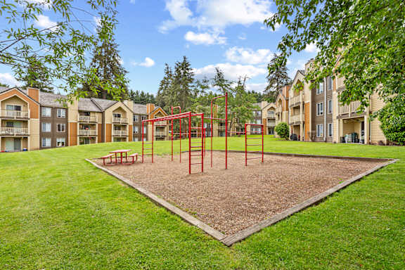 A playground with a red swing set in the middle of a grassy area at MonteVista Apartments, Beaverton, 97007