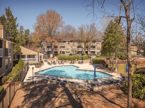 A swimming pool surrounded by trees and chairs.